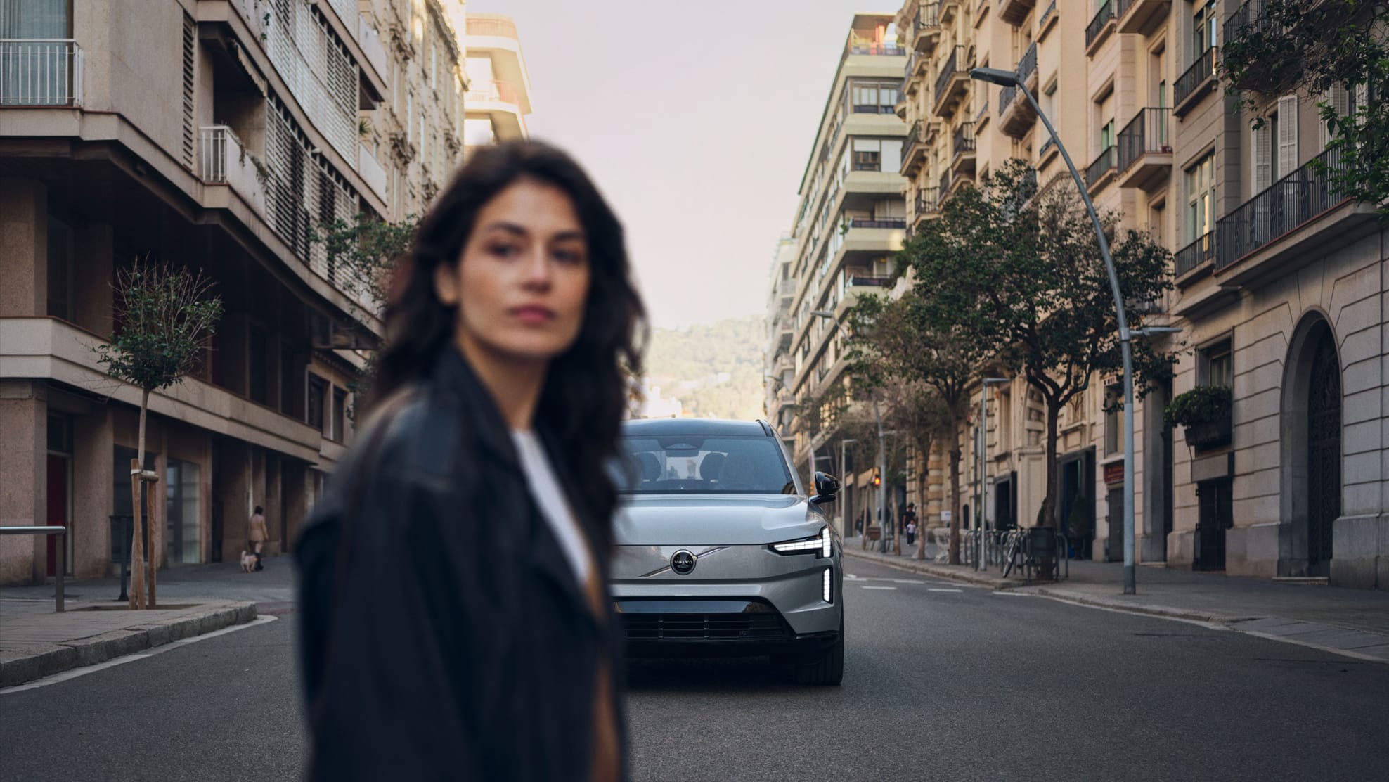 A woman turns towards the camera on a quiet city street at dusk, a silver Volvo EX90 waiting in the road behind her – the still that opens the Stendahls showreel.