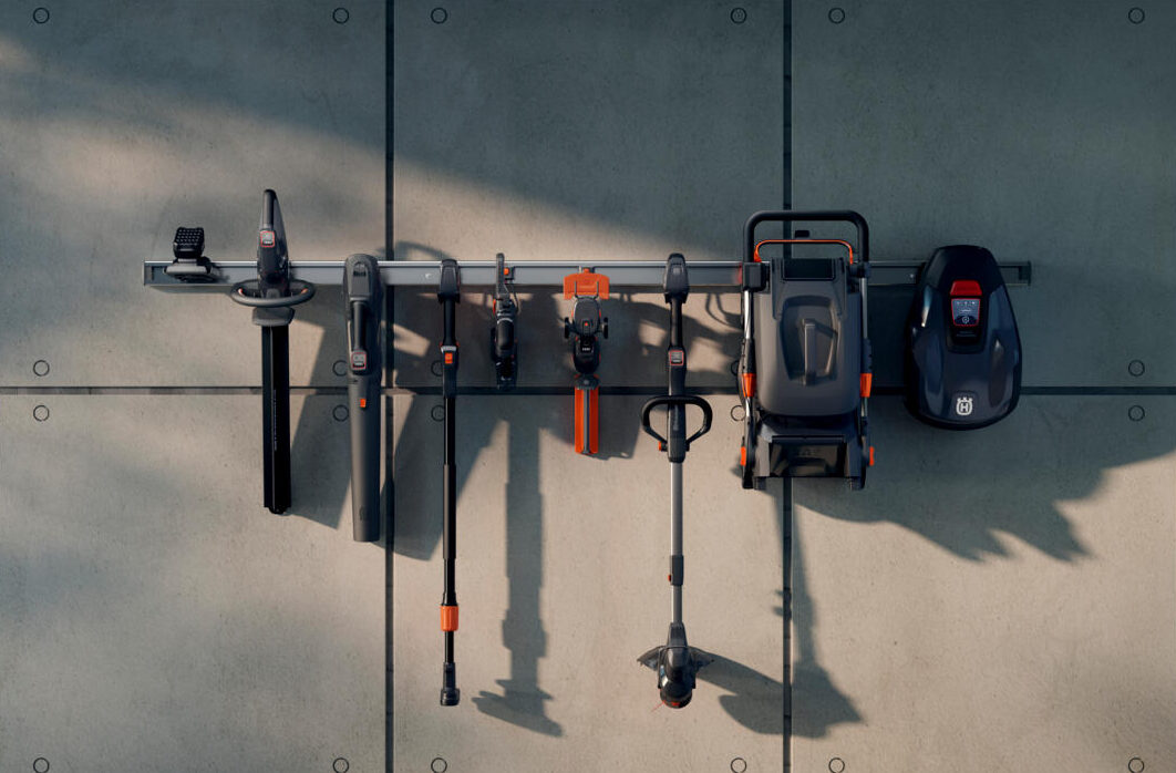 A rack of battery-powered garden tools mounted on a concrete wall, orange details standing out in the raking light.