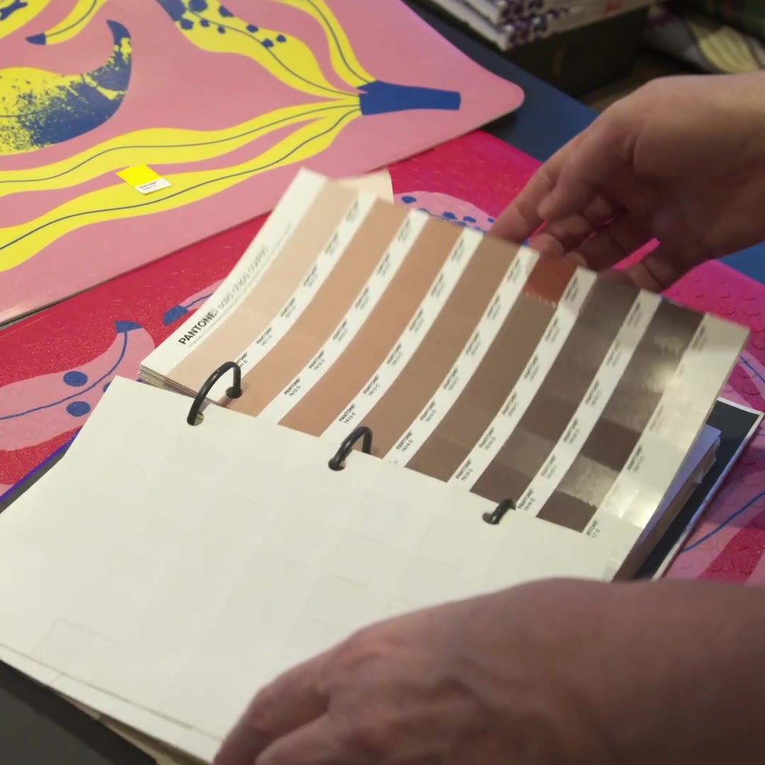 Designer Lotta Kühlhorn leafing through Pantone swatches over the banana-patterned mats in her studio – campaign short.