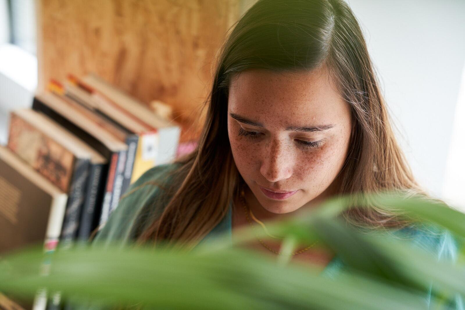 Colleague reading at a studio bookshelf, framed by green leaves in the foreground.