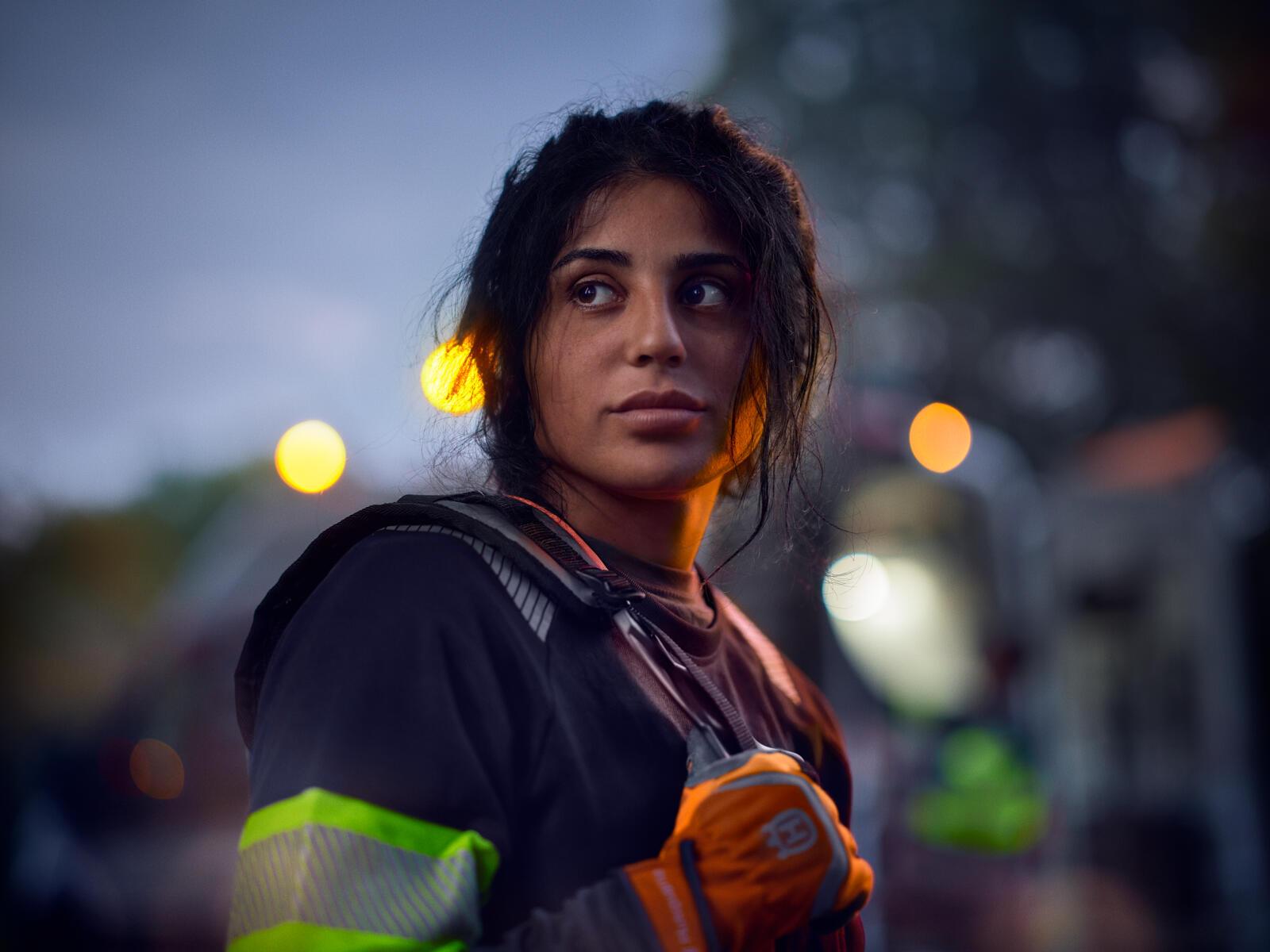 A landscaper in hi-vis workwear at dusk, lit by warm street lights – the human face of Husqvarna’s battery campaign.
