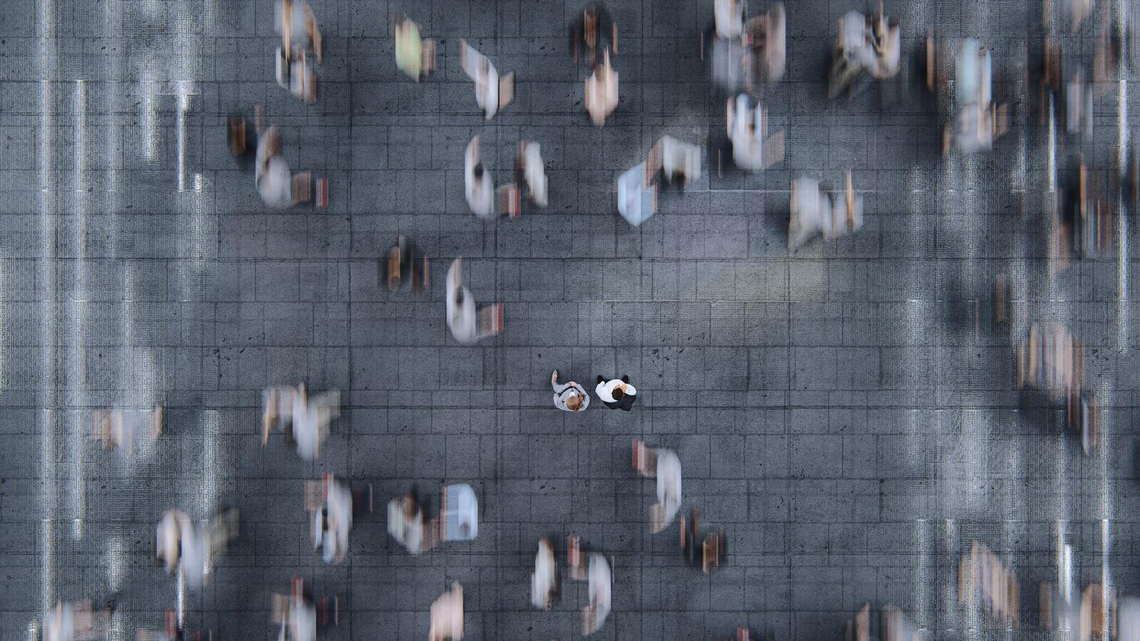 Aerial view of a square where two people stand still in a blurred, moving crowd.