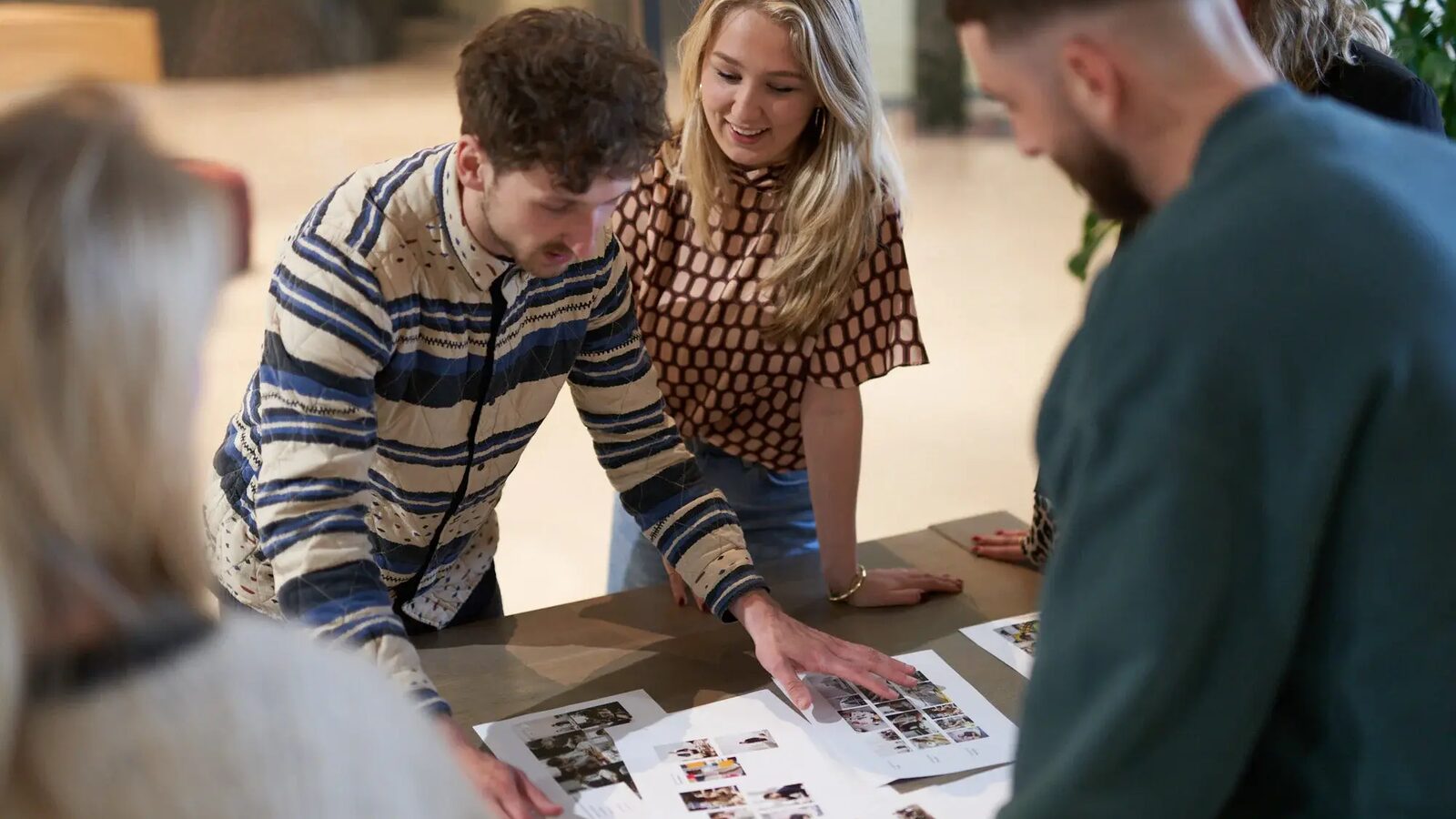 Four people lean over a table covered in printed brand sheets, comparing layouts side by side.