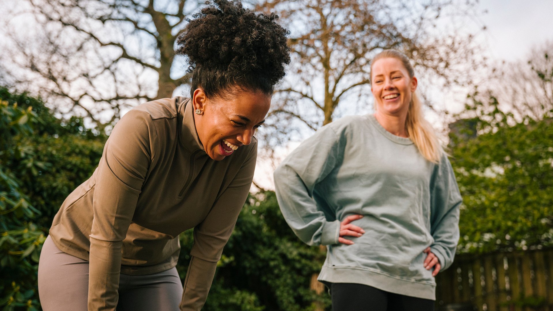 Two women laughing mid-workout in a park – the campaign's warm, unpretentious take on getting started.